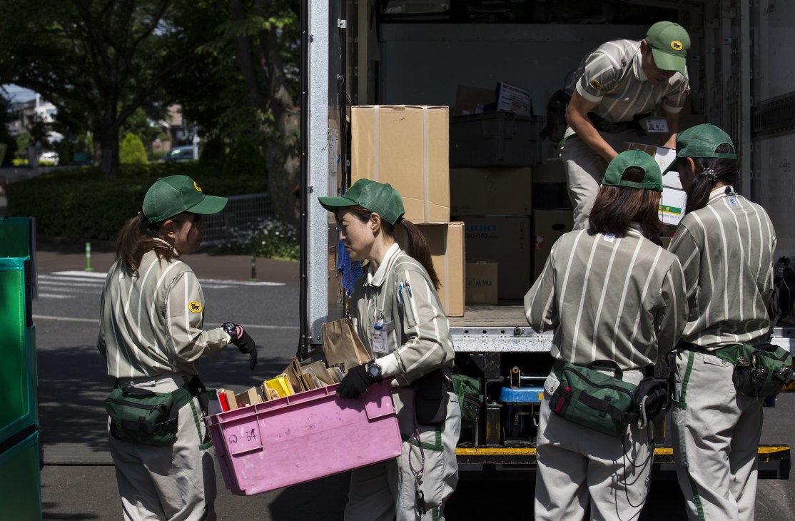 Yamato Transport delivery workers in green caps and tan uniforms loading cardboard boxes into a delivery van.