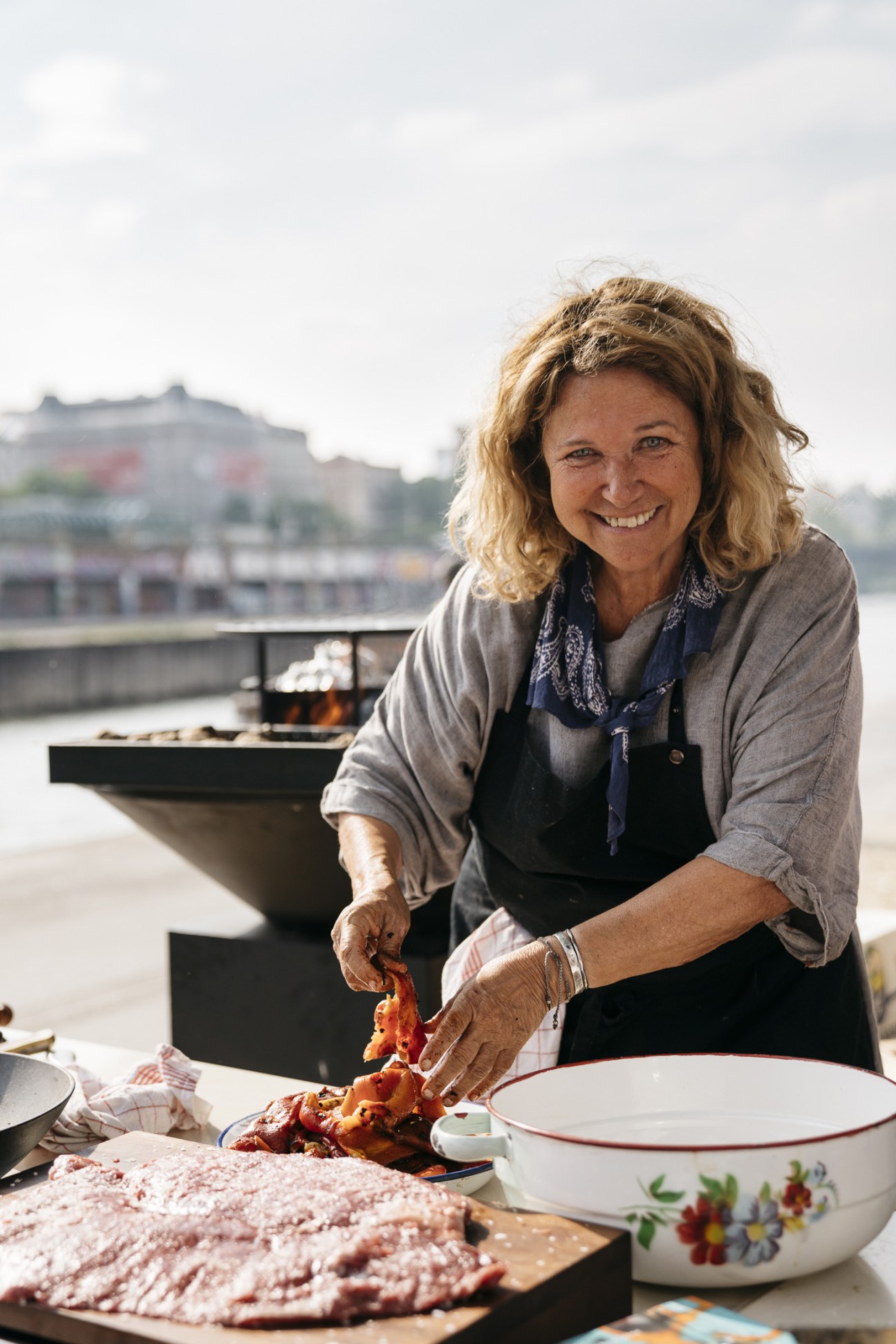 Chef Haya Molcho prepares food at Tel Aviv Beach on Vienna's Danube Canal with boats in the background.