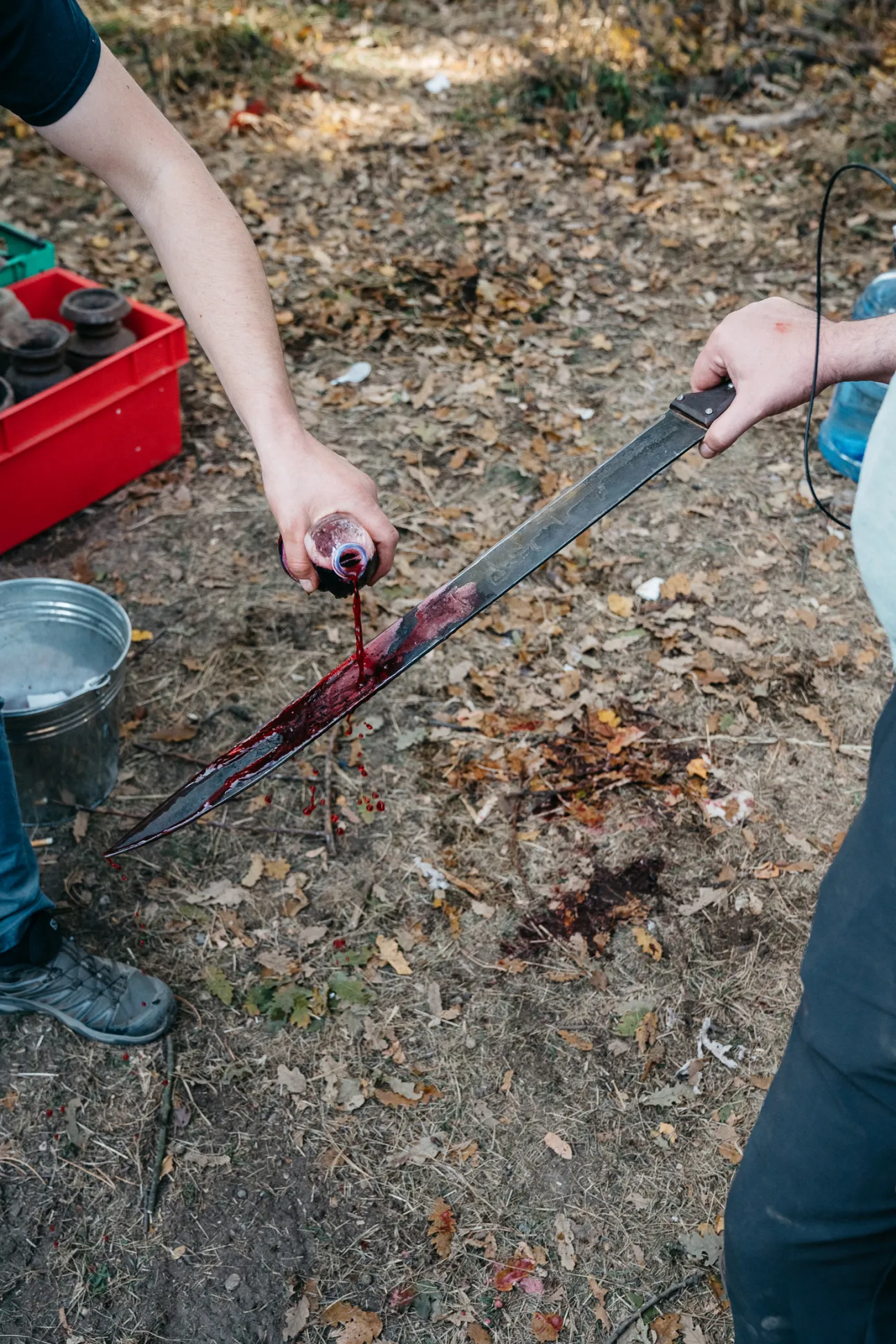 Hands applying fake blood to a sword prop on the ground during The Barbarians filming.