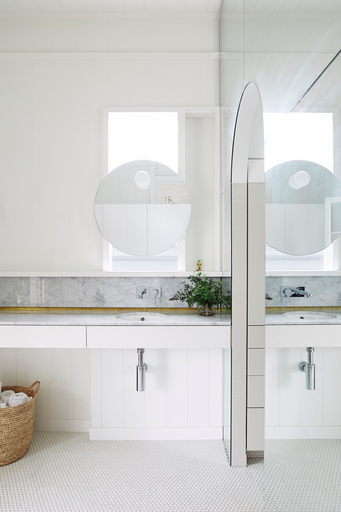 Modern bathroom with dual circular mirrors, marble countertop, white cabinetry and minimal fixtures.