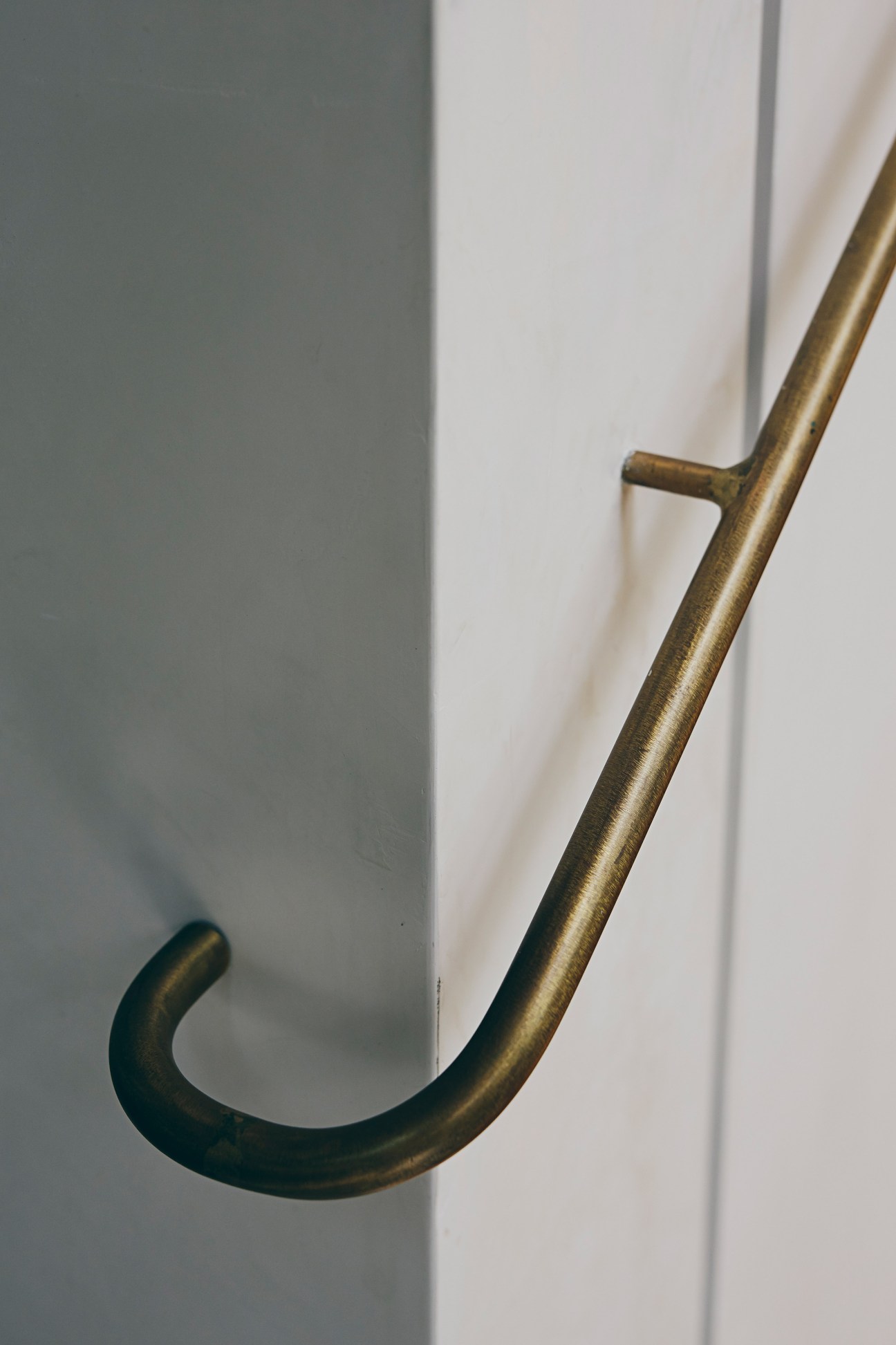 Close-up of a curved brass rail mounted on a white wall.