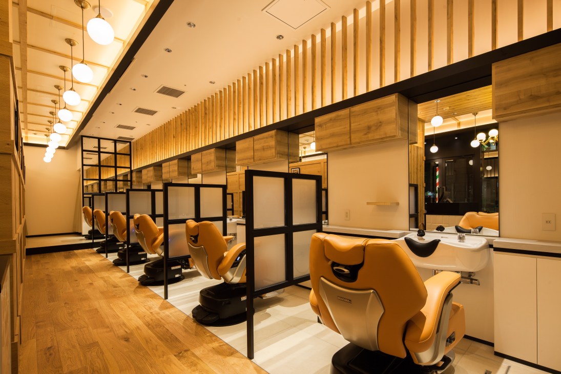 Modern barber salon interior with orange chairs separated by black-framed frosted glass partitions and wooden ceiling details.