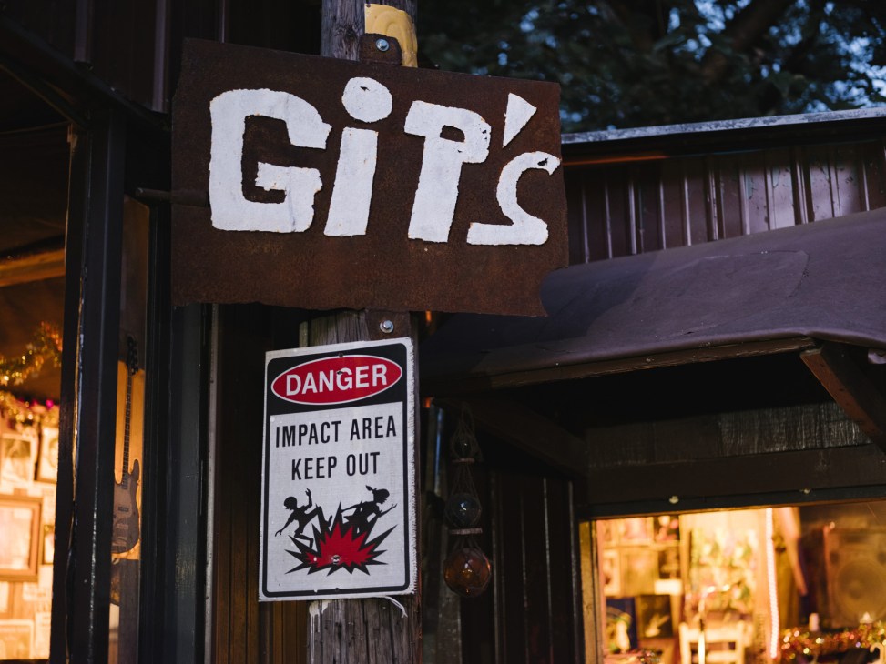 Gip's Place juke joint sign with weathered white lettering on brown metal, with a humorous danger sign below.