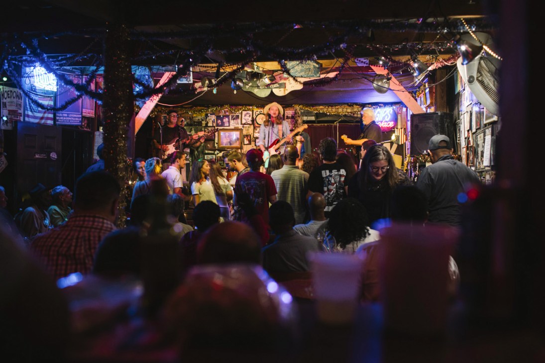Musicians performing on stage at Gip's Place juke joint with a diverse crowd of patrons dancing and watching.