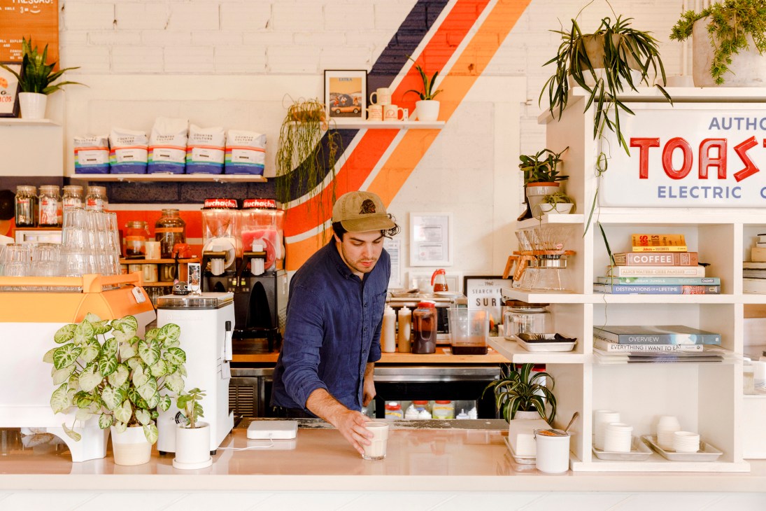Barista in blue shirt and cap preparing drinks behind coffee counter at Muchacho