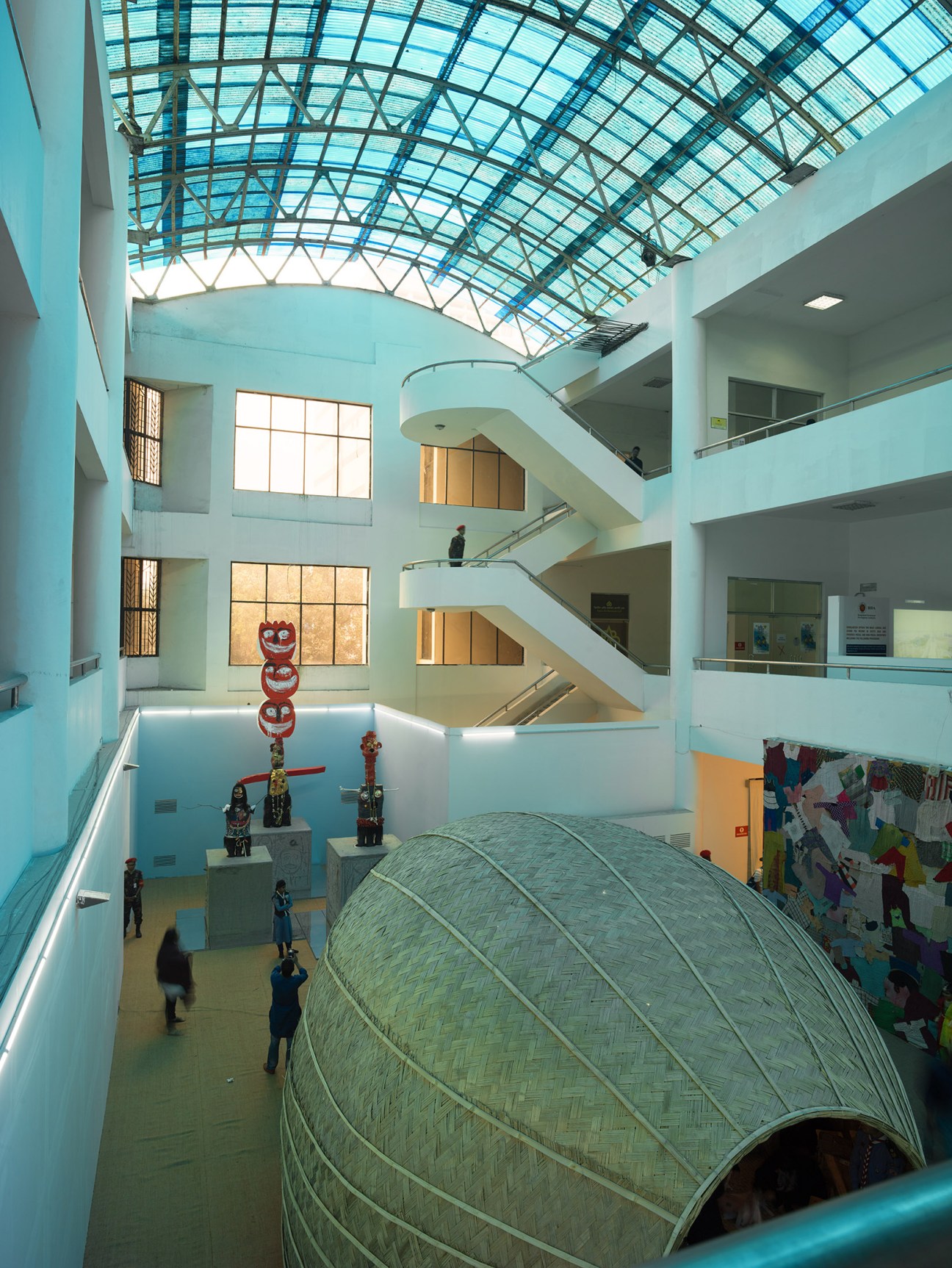 Bright modernist interior of Shilpakala Academy with skylight, spiral staircase, and woven installation art.
