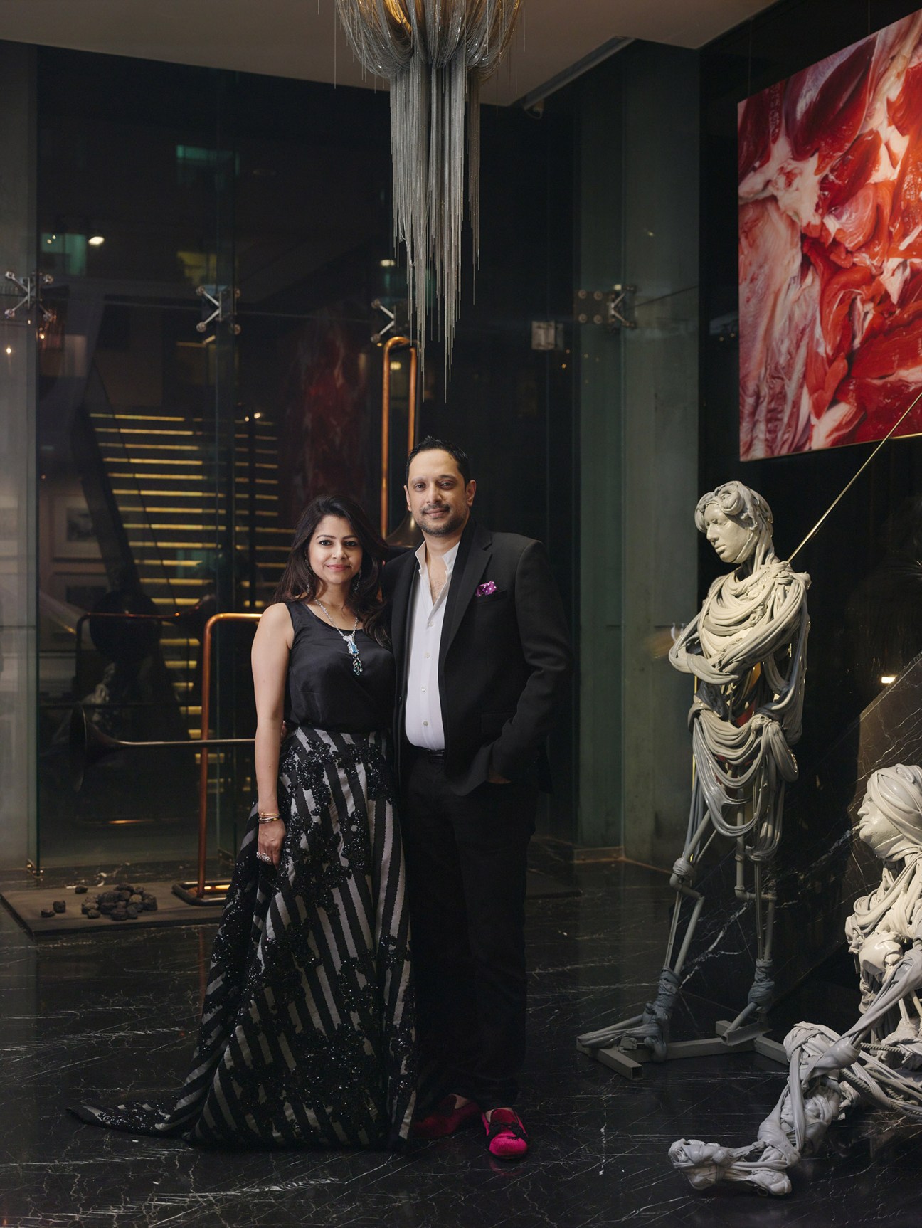 Nadia and Rajeeb Samdani stand in an art gallery beside a white classical bust sculpture.