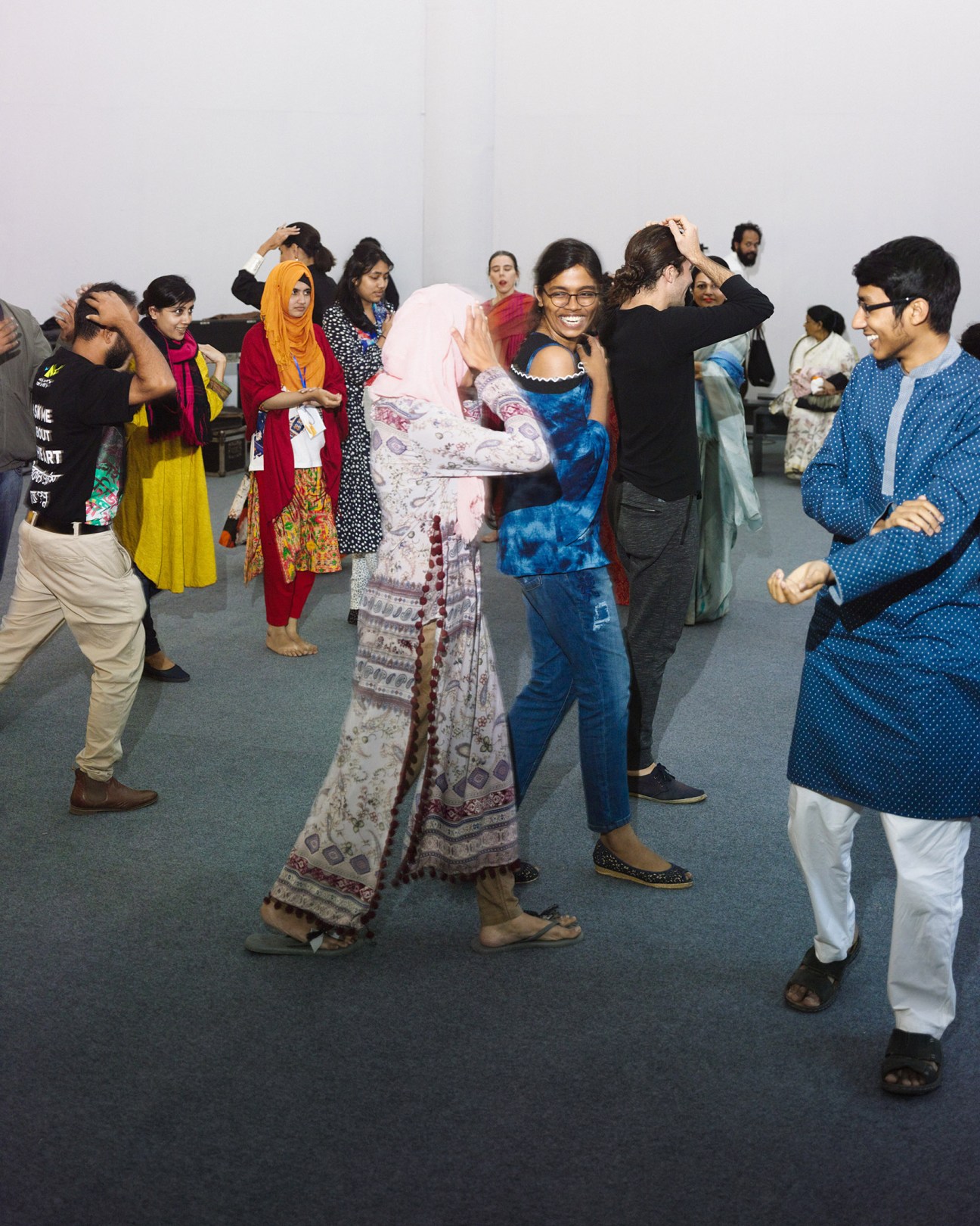 Group of visitors dancing and celebrating at the Dhaka Art Summit in a white gallery space.
