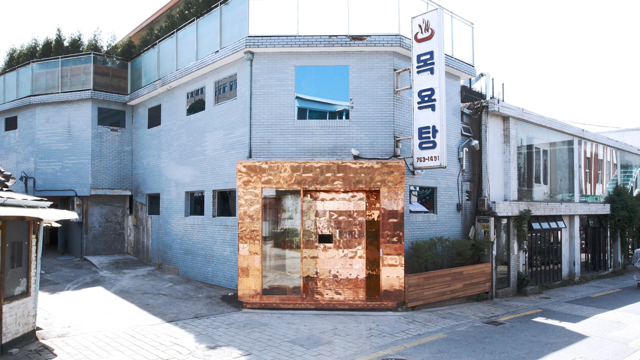 Gentle Monster's copper-framed bathhouse shop storefront in Bukchon, Seoul, surrounded by white-brick buildings.