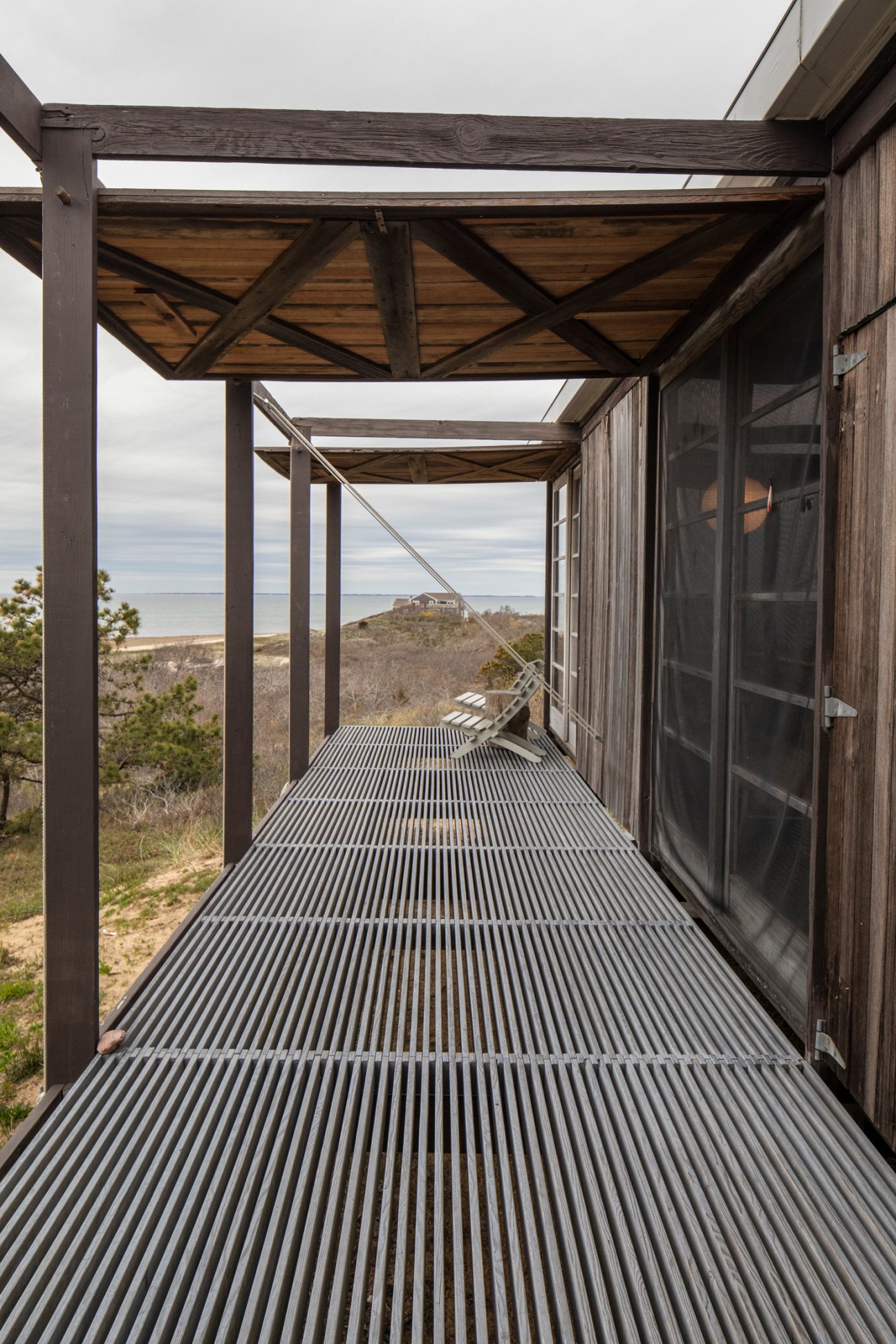 Wooden veranda with metal frame pergola overlooking coastal dunes and ocean at Hatch Cottage.