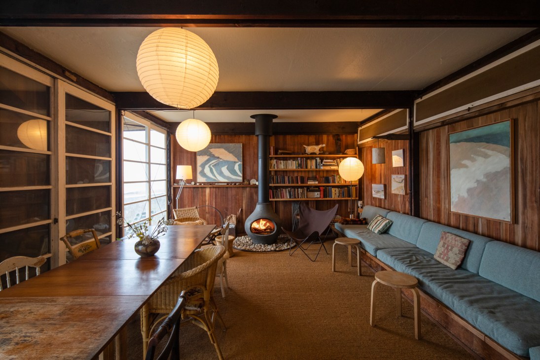 Interior of Hatch Cottage dining area with wood paneling, fireplace, blue sofa, and paper lantern lights.