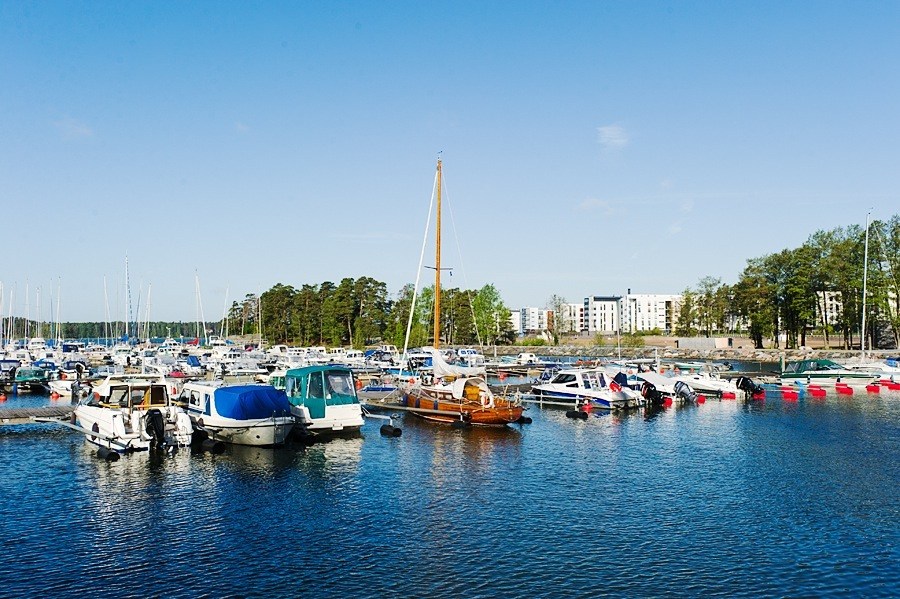 Helsinki waterfront with moored sailboats and residential buildings in background under clear sky.
