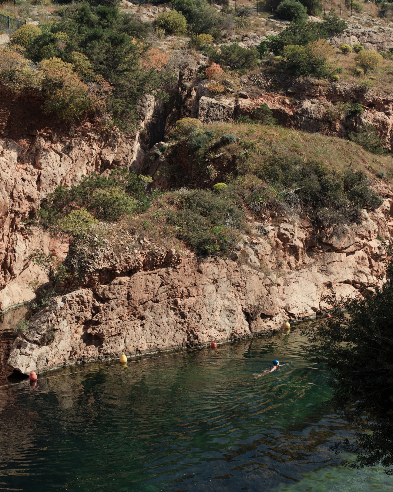 Swimmers enjoy the clear turquoise waters of Lake Vouliagmeni surrounded by rocky cliffs and Mediterranean vegetation.