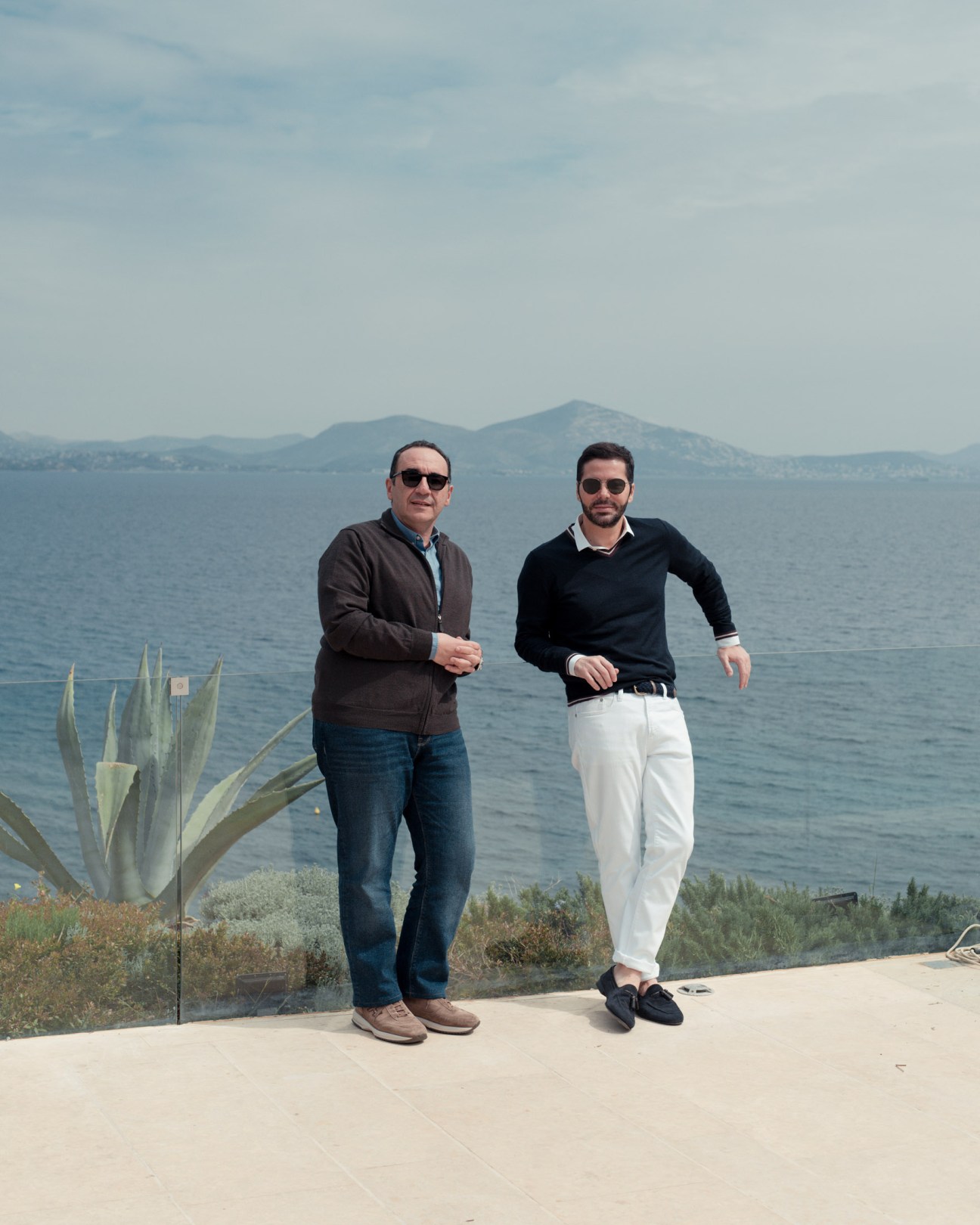 Two men jogging along a terrace overlooking the Aegean Sea with mountains in the distance.
