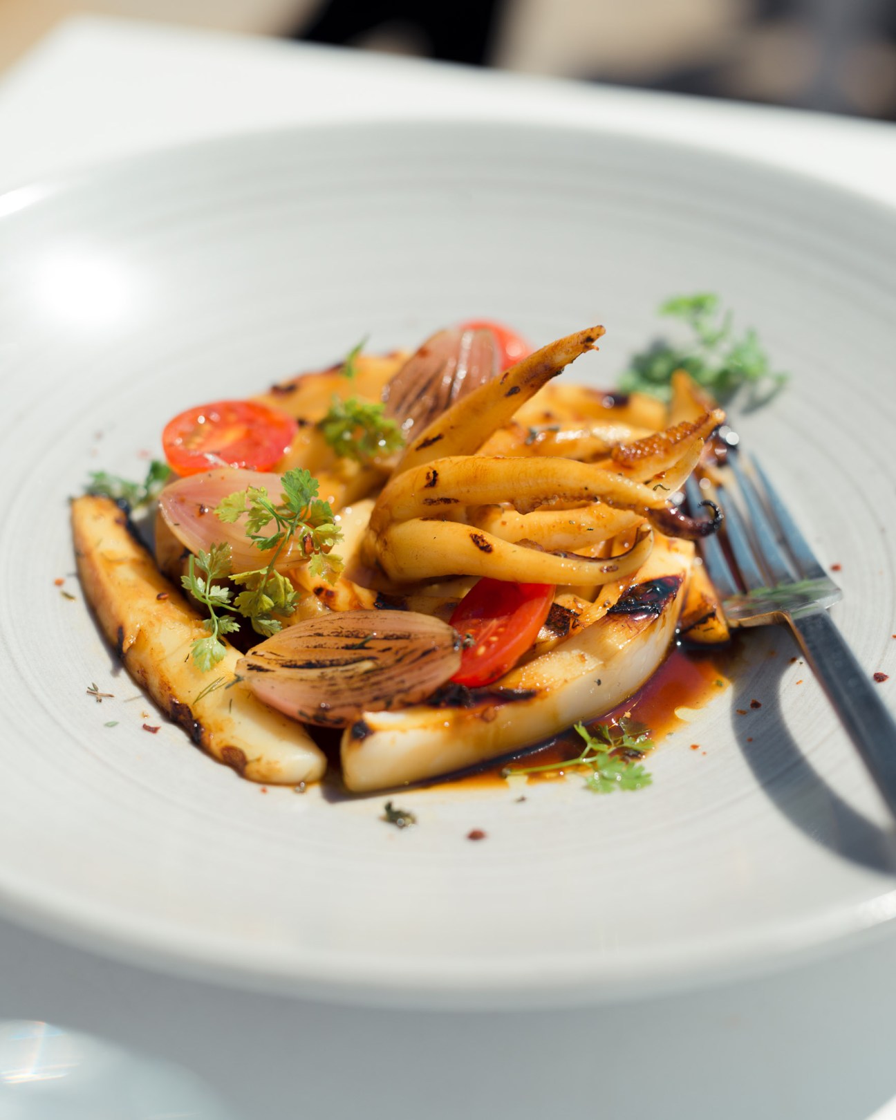 Grilled seafood dish with squid, tomato and herbs on white plate at BlueFish restaurant