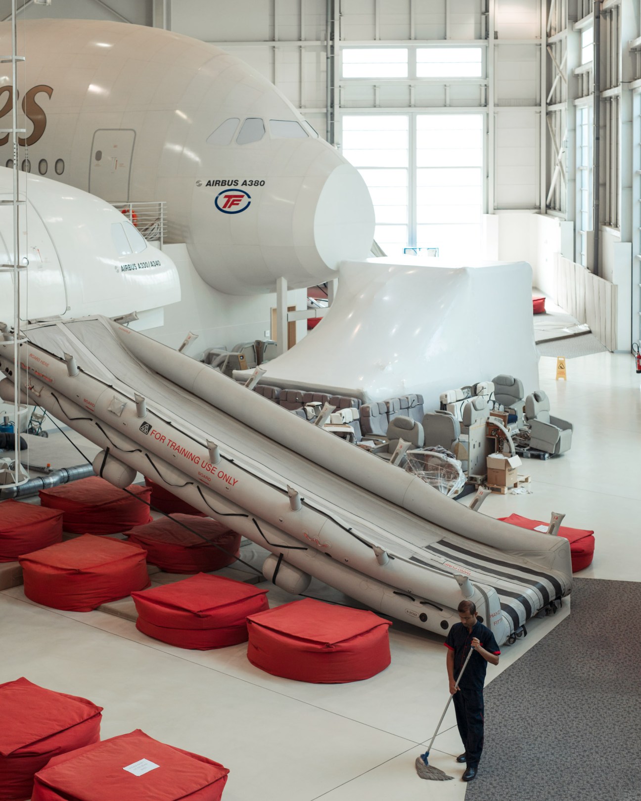 Training mock-ups of Airbus A330 and A380 aircraft fuselages in a bright hangar with red safety cushions.