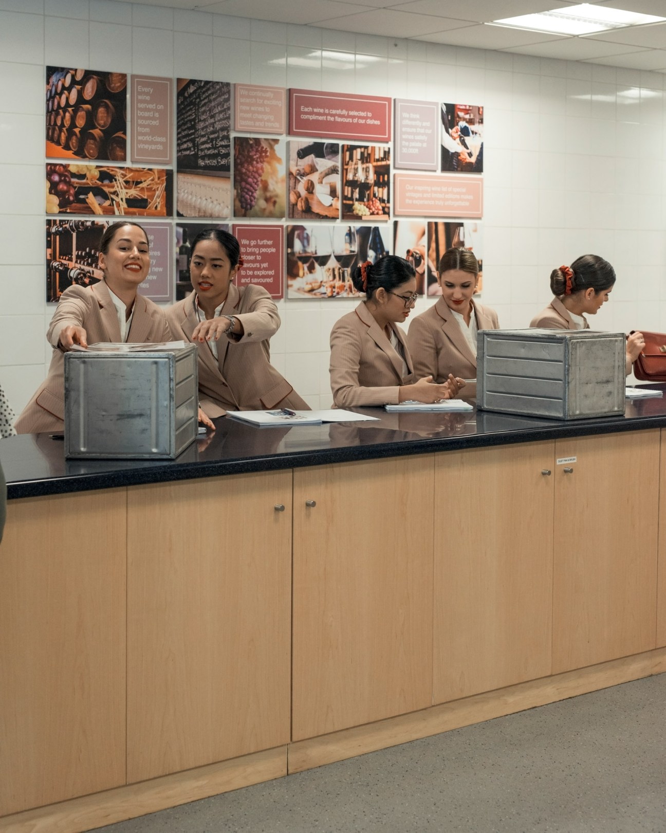 Emirates flight attendant trainees in beige uniforms study meal carts at training facility.
