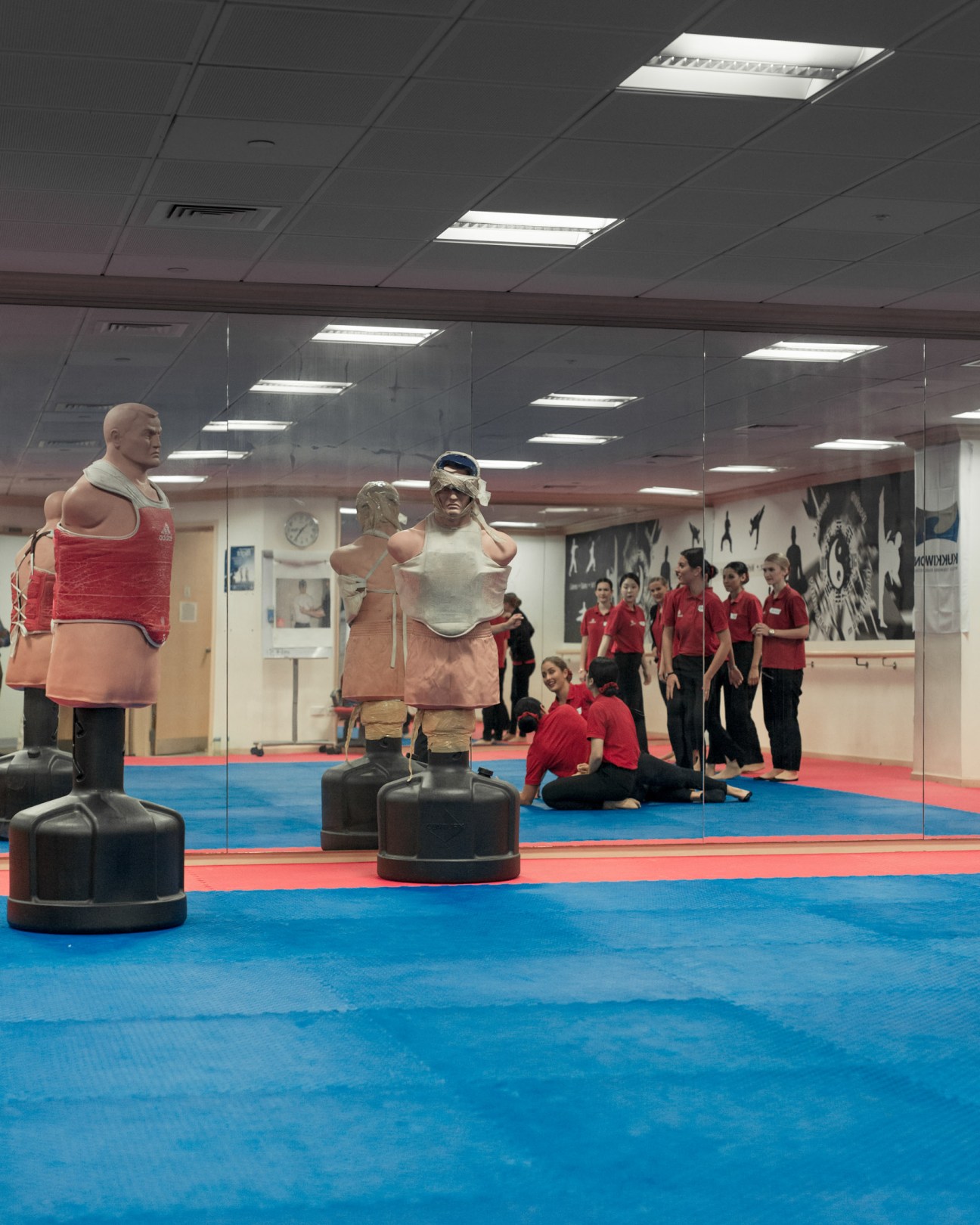 Emirates flight attendant trainees in red uniforms practicing self-defence with punching bags in a training studio.