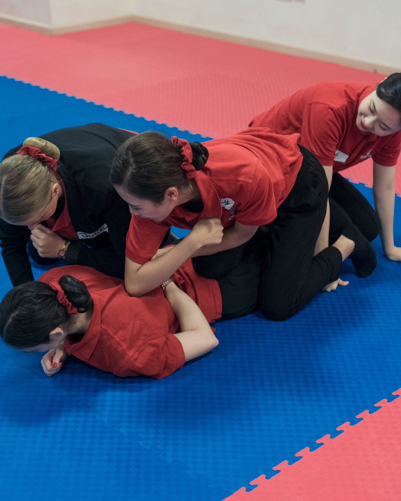 Emirates flight attendants in red uniforms practice tae kwon do on a blue and red padded mat.