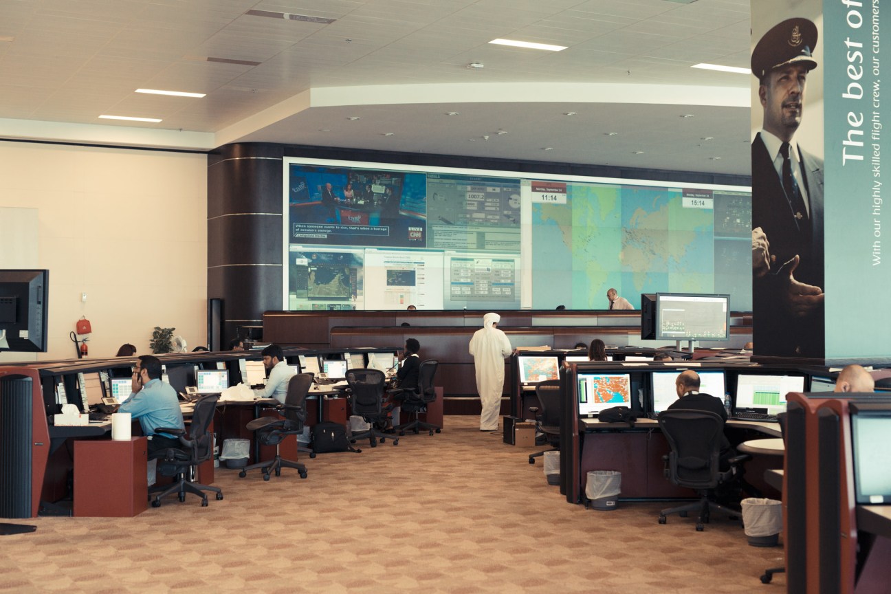 Emirates Network Control center with staff monitoring flights at computer workstations beneath large display screens.