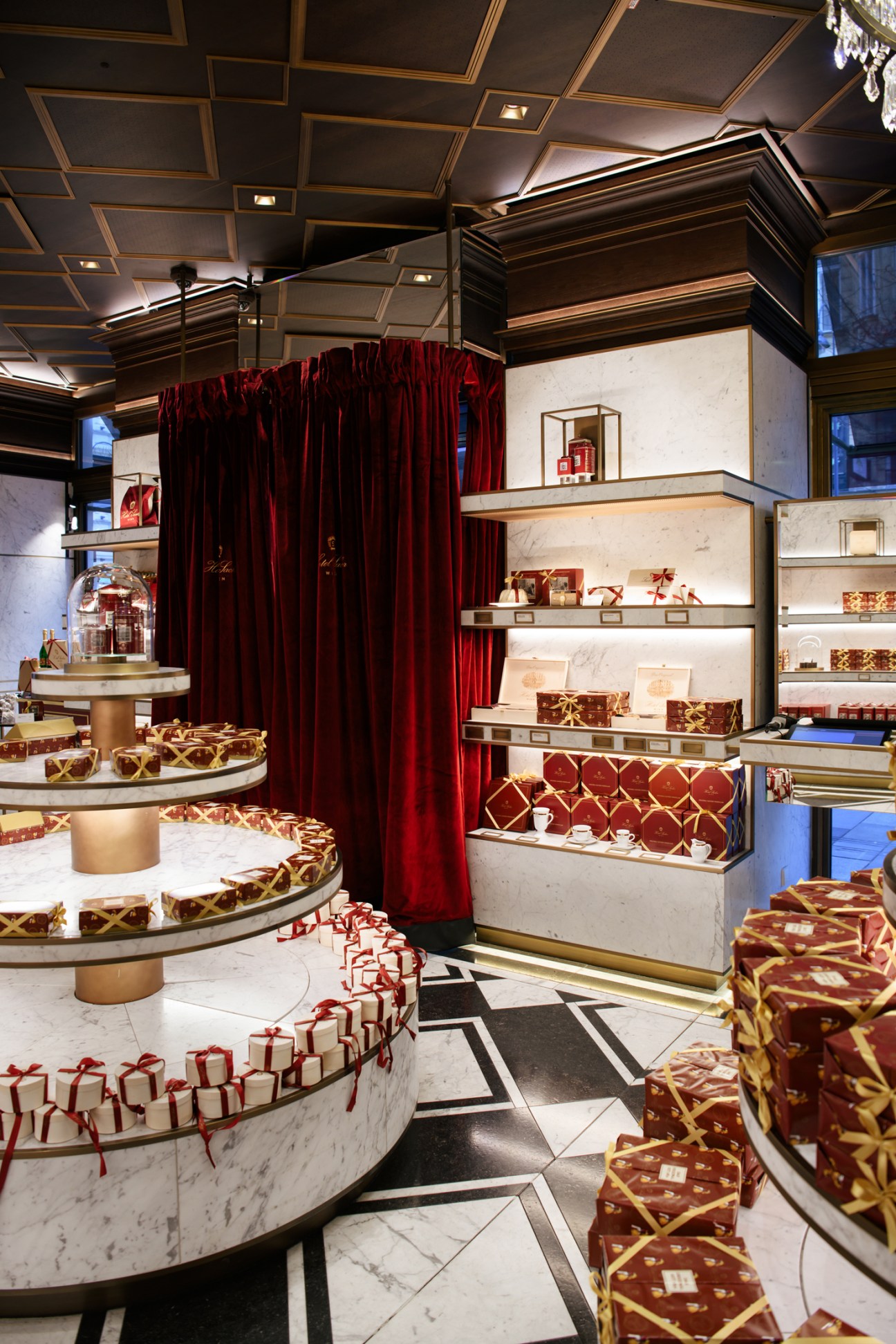 Elegant display cases with gift boxes and confectionery in an upscale patisserie with red curtains and ornate ceiling