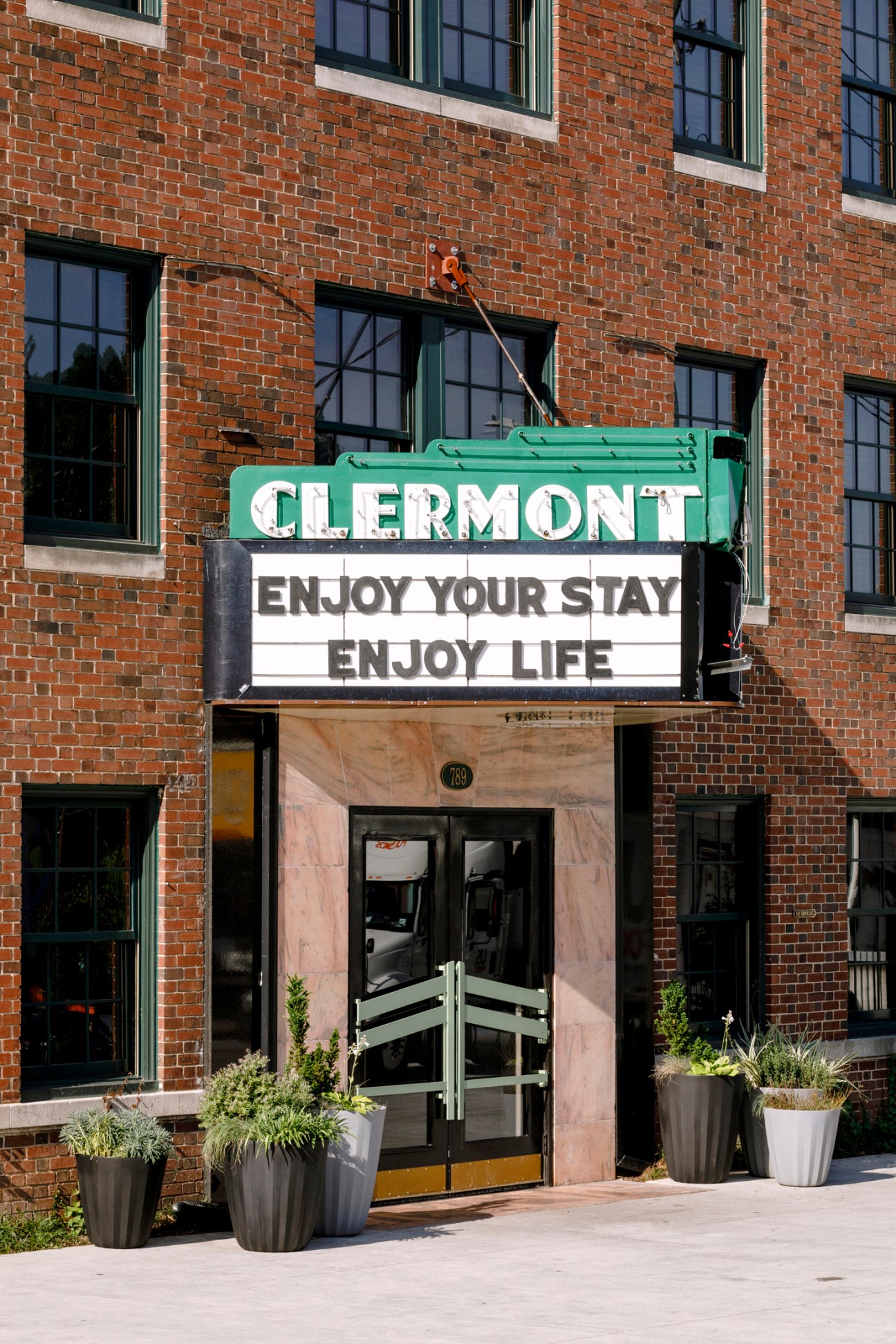 Hotel Clermont exterior signage with green marquee reading 'CLERMONT' and 'ENJOY YOUR STAY ENJOY LIFE'