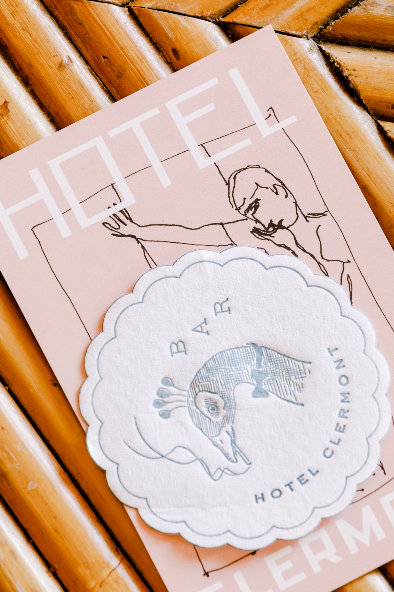 Pink branded materials with Hotel Clermont logo and illustrated character design on wooden surface