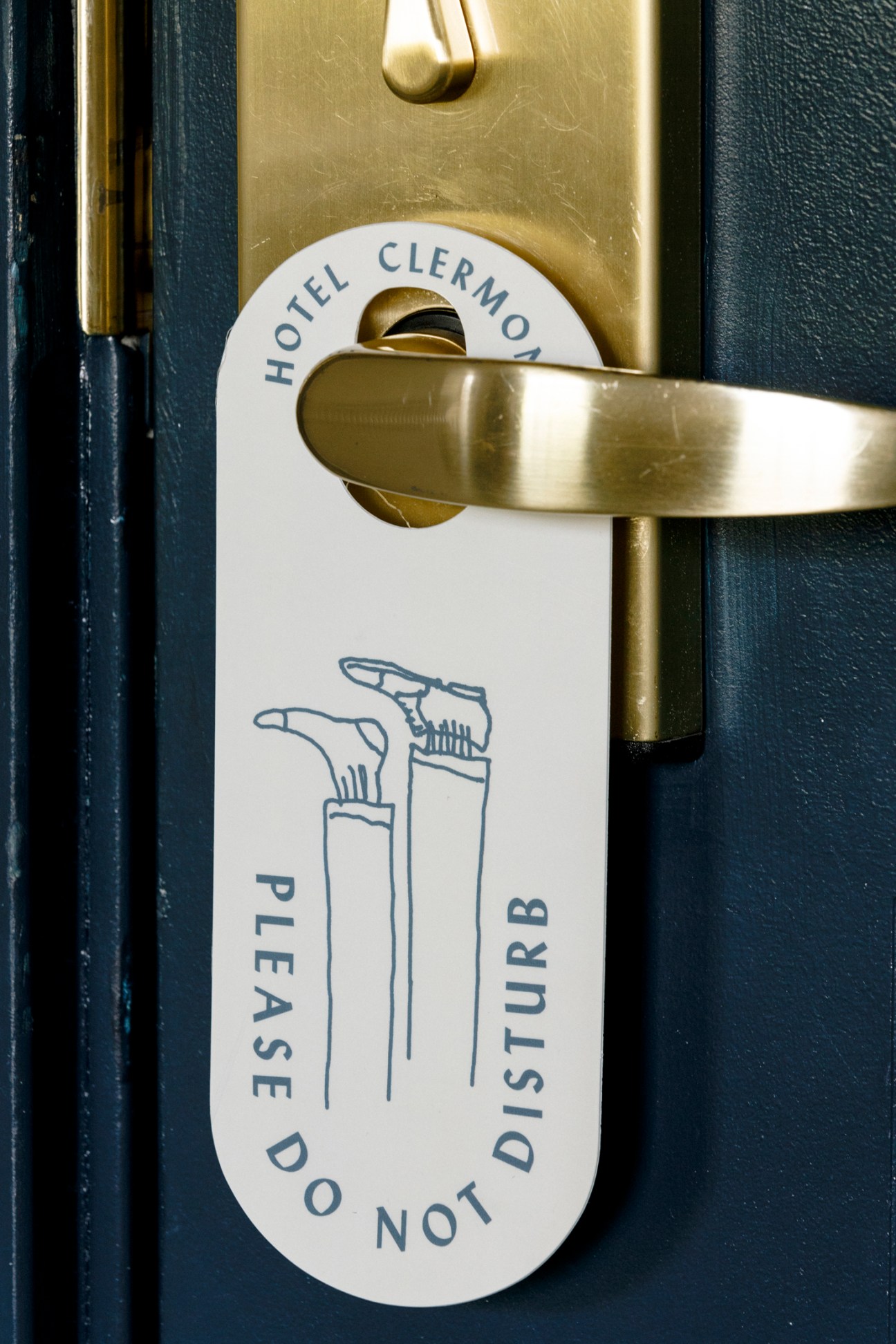 White do not disturb door hanger with toothbrush illustration and Hotel Clermont branding on gold door handle