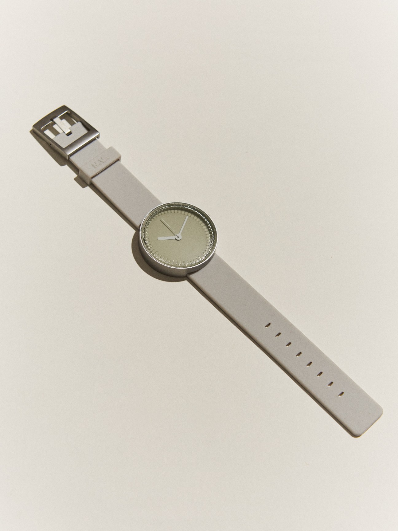 Watch by Nava Design with minimalist face and grey leather strap on beige background.