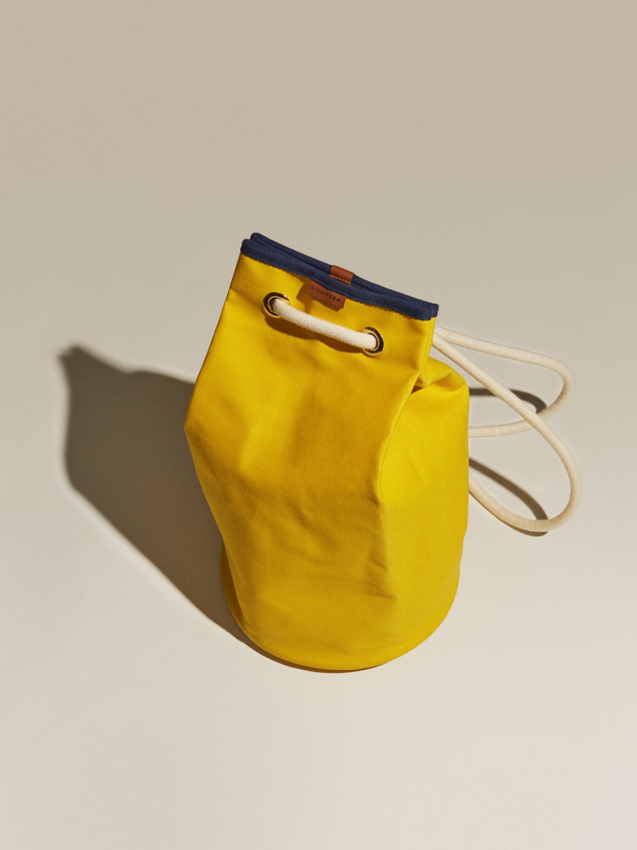 Bright yellow drawstring bag by L/Uniform with navy trim and cream rope handles.