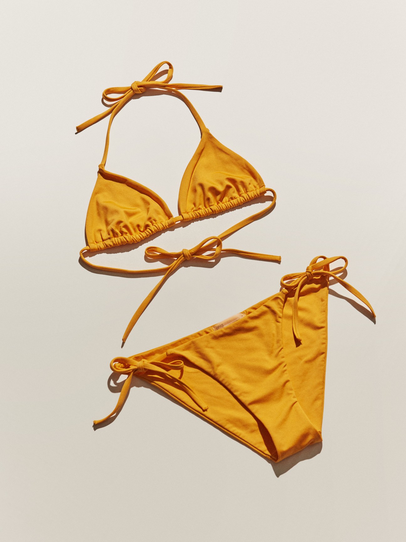 Golden yellow bikini with tie straps laid flat on a neutral background.