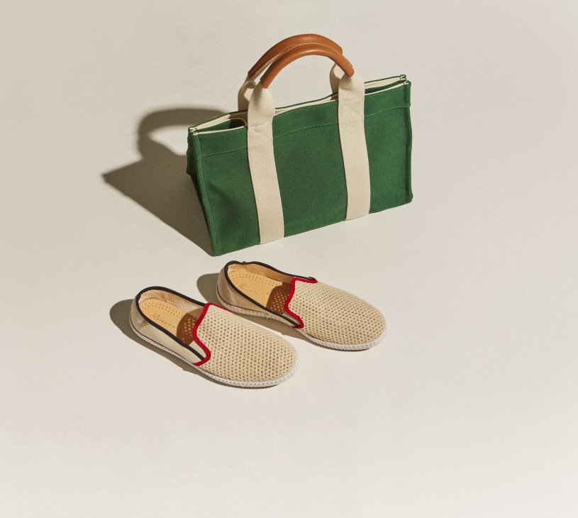 Green canvas tote bag with cream handles and leather accents, paired with beige mesh slip-on shoes with red trim.