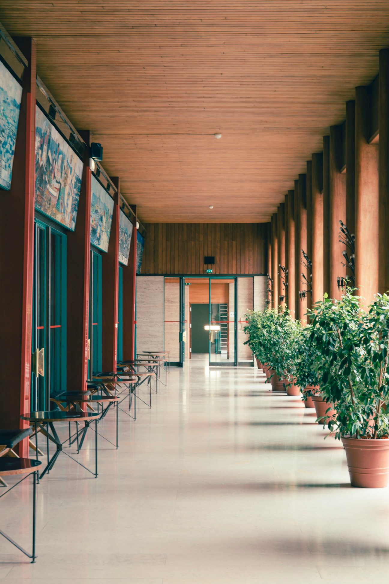 Long gallery corridor with wood ceiling, black leather chairs, potted plants, and turquoise window frames