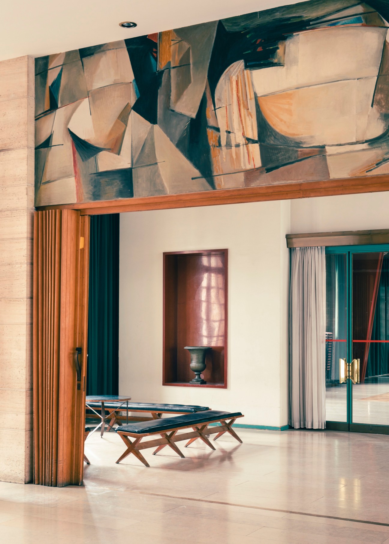 Modern interior with abstract ceiling mural, X-frame benches, wall niche with lamp, and curtained doorway