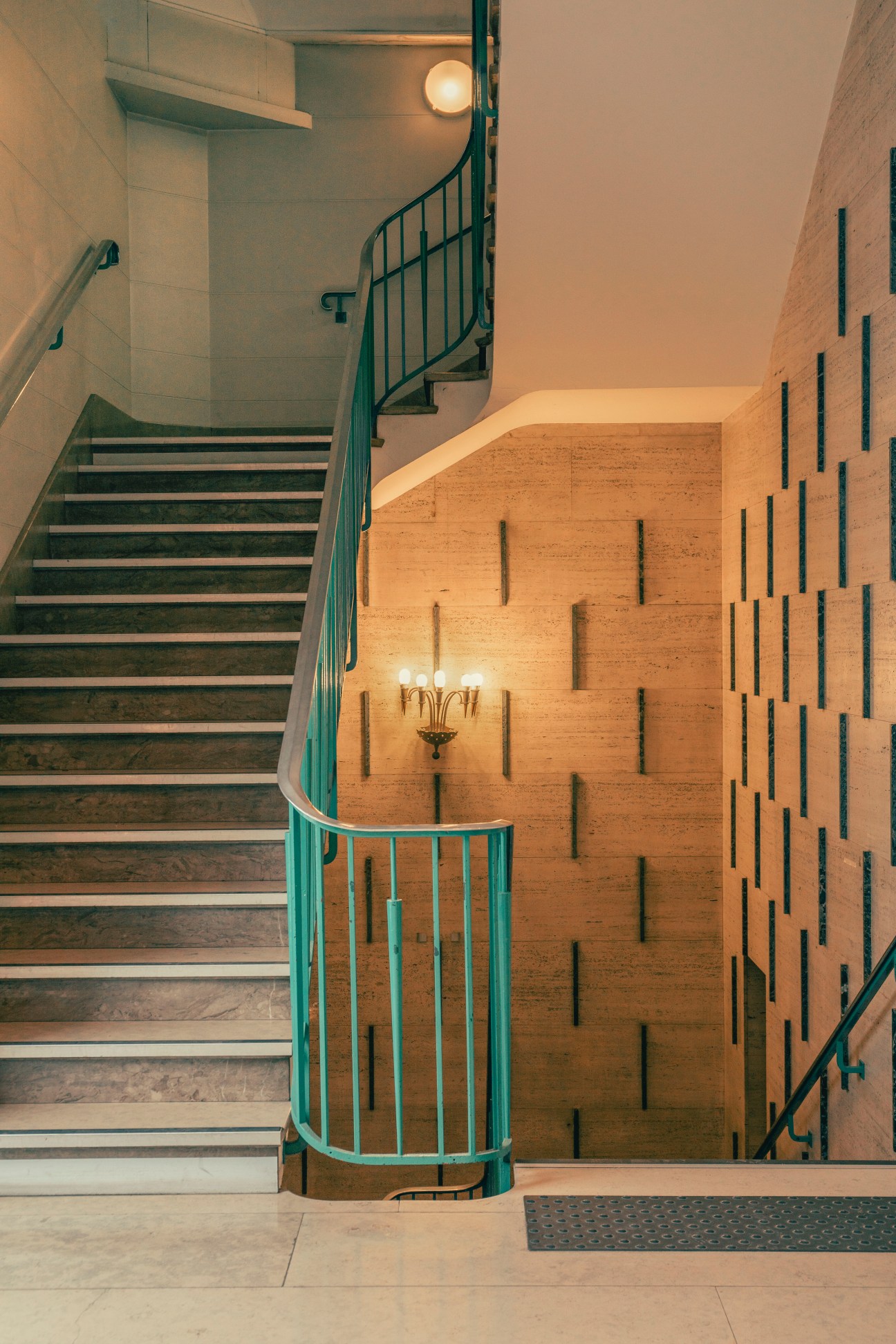 Curved staircase with turquoise metal railings and geometric wood wall panels in modernist interior