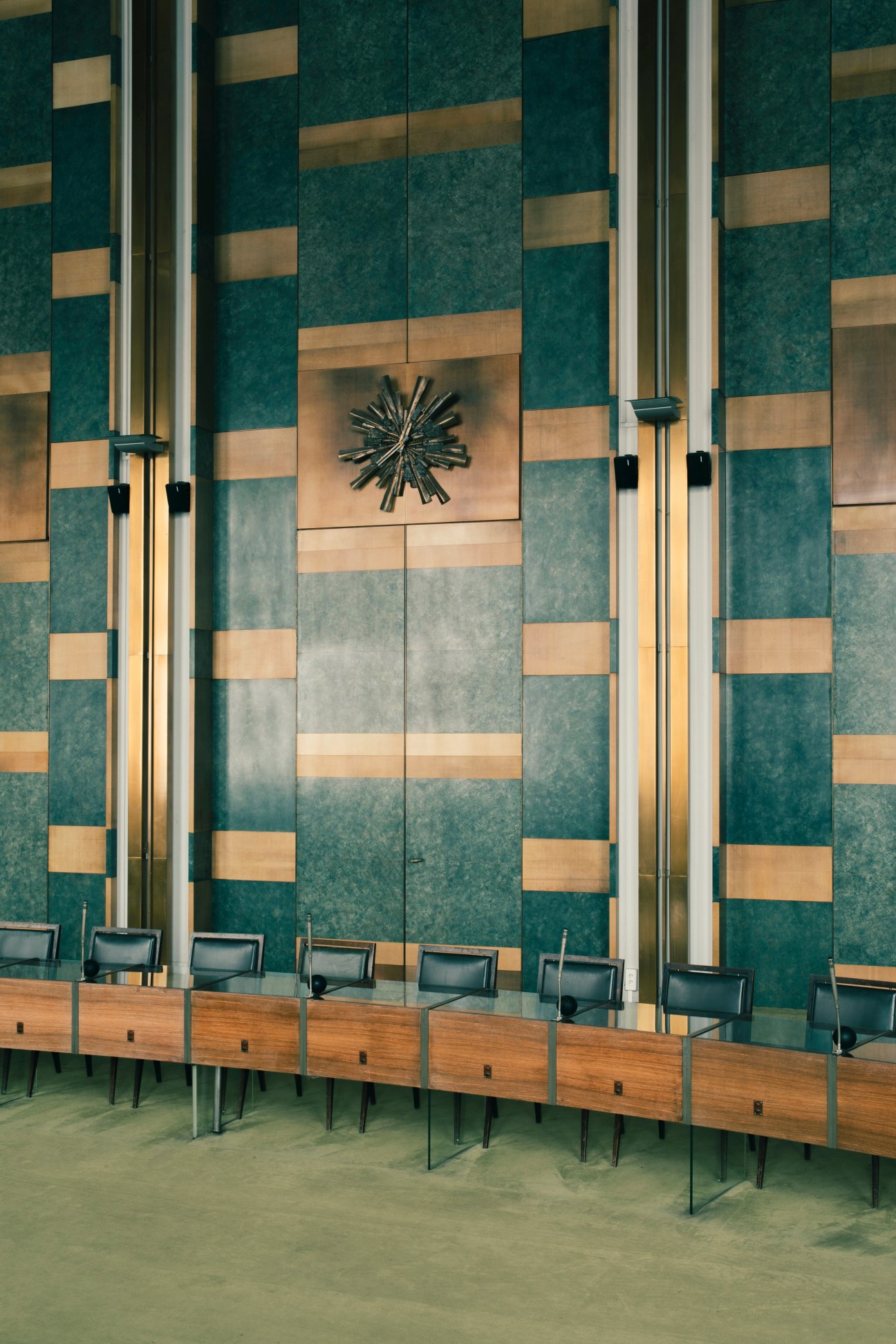 Tall geometric doors with teal and bronze panels featuring a starburst medallion sculpture by Jean-Pierre Demarchi