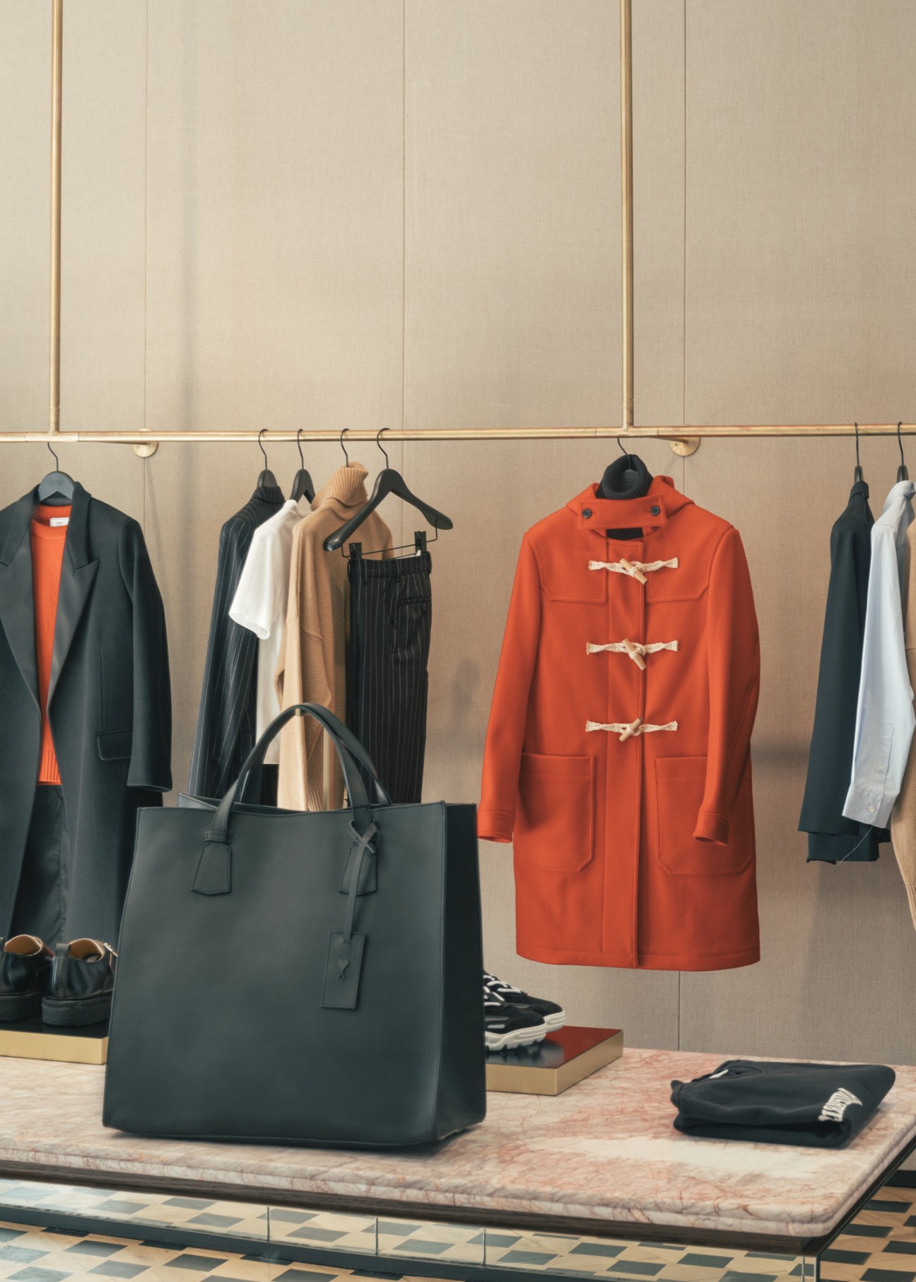 Ami women's shop display featuring a red duffle coat, black blazer, and tote bag on a marble table.