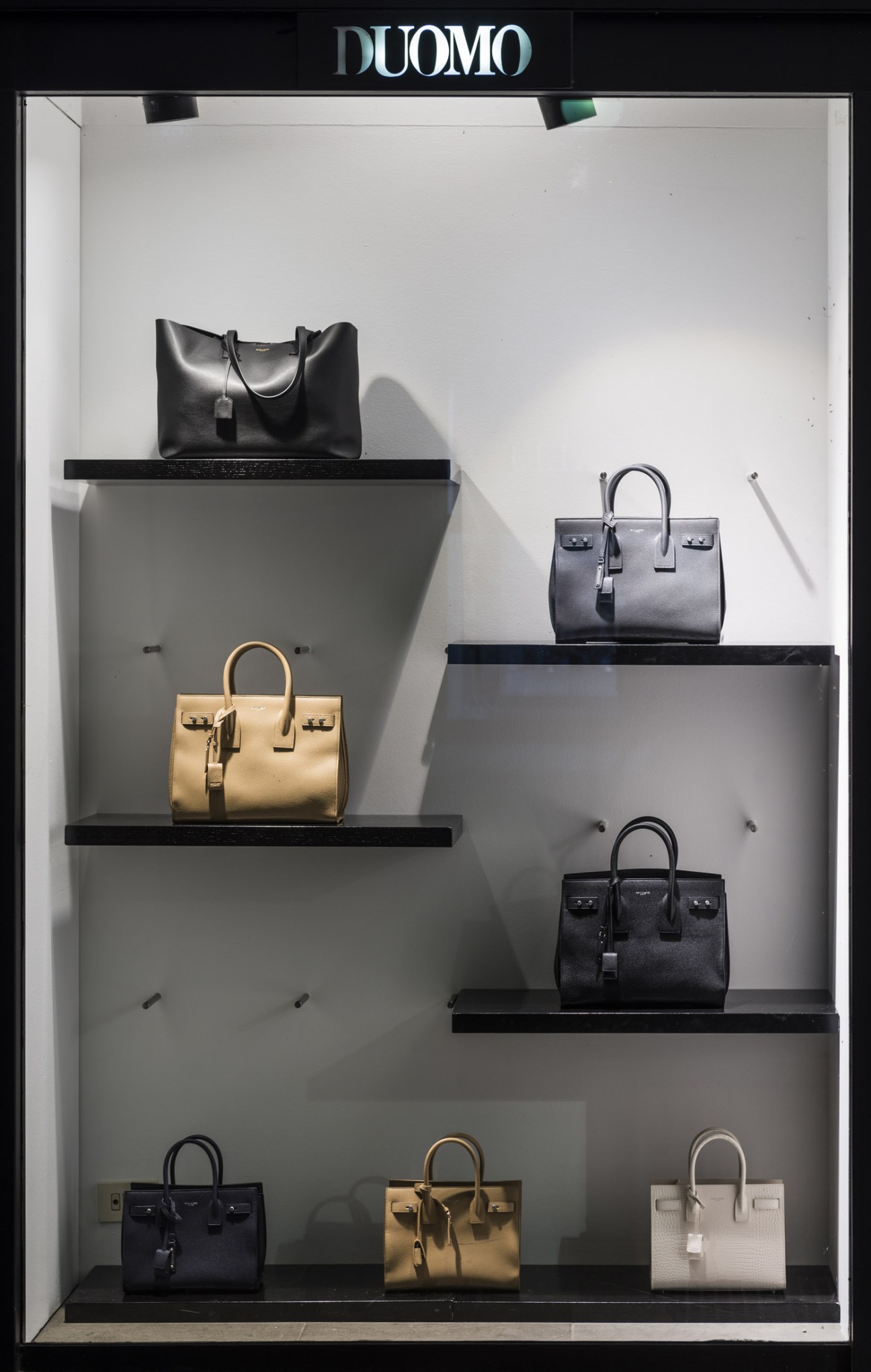 Il Duomo boutique window display featuring luxury handbags on black shelves against white walls.