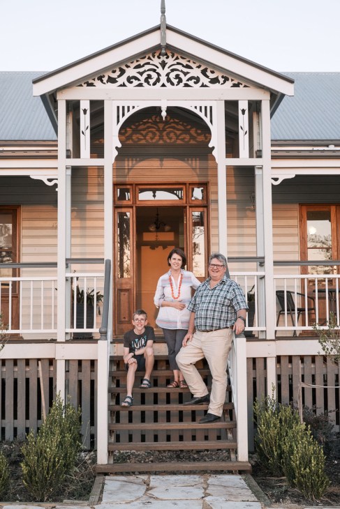 Peter Wilson and his family stand on the porch of a white Queenslander-style house with ornate trim.
