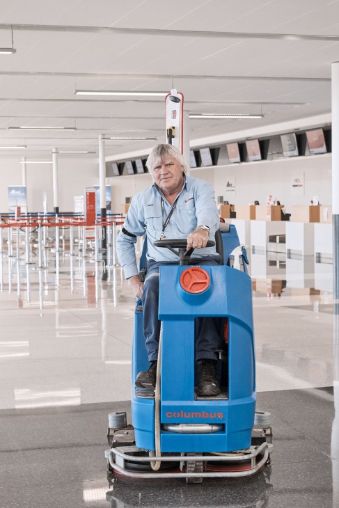 Airport worker operating a blue Columbus floor cleaning machine in Wellcamp's departures hall.