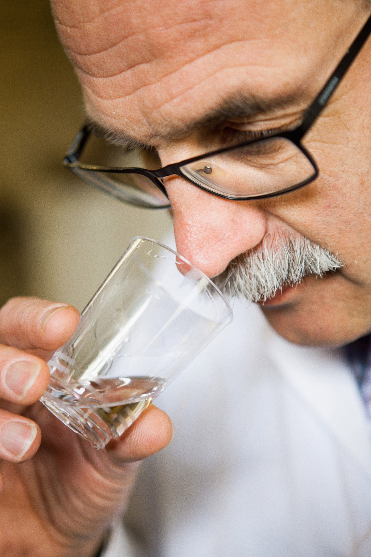 Man with glasses tasting clear spirit from a small glass.