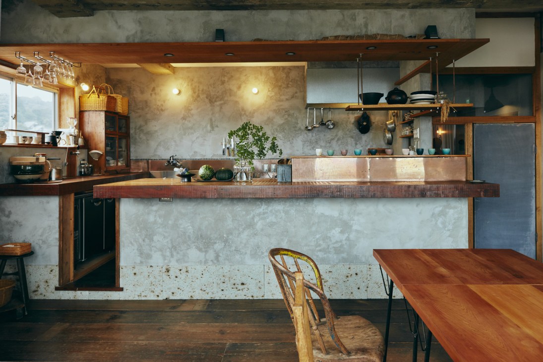 Hotel Aiaoi's kitchen and dining room with wooden beams, concrete walls, and open shelving.