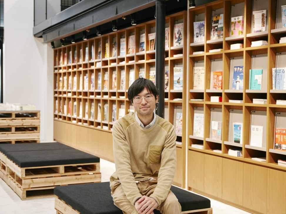 Kengo Takeda, project leader, sits in front of wooden bookshelves at Bunkitsu bookshop in Tokyo.