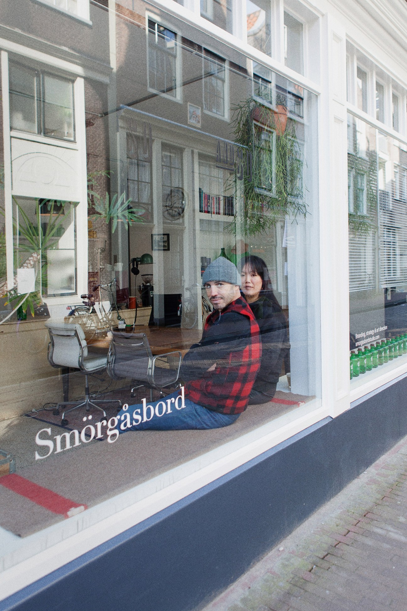 Dylan Griffith and Nathalie Ji Yun Kranenburg sit at a desk inside the Smörgåsbord design studio, visible through large storefront windows.