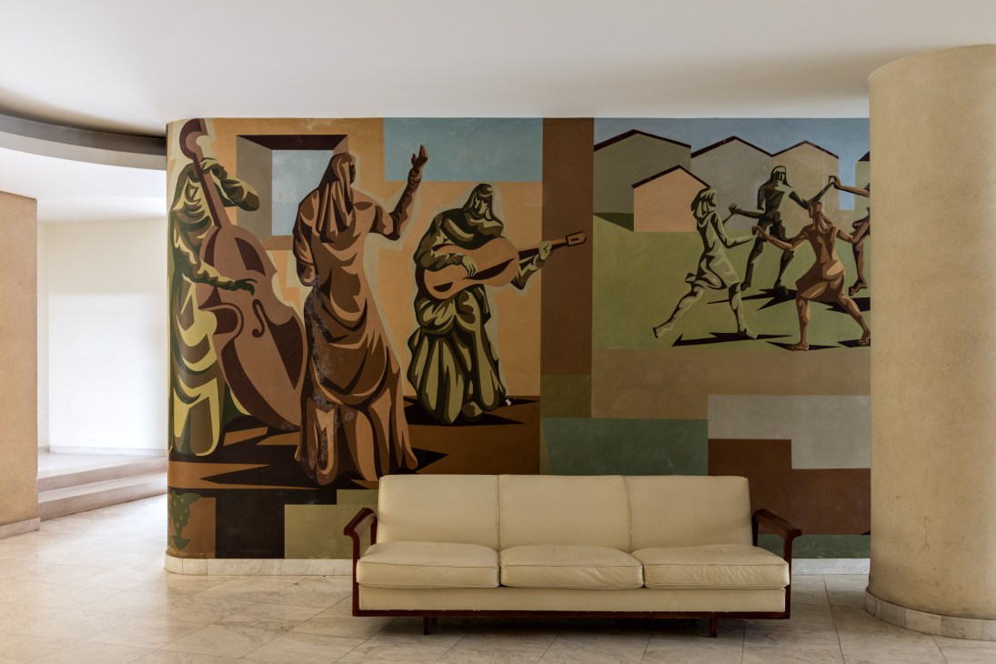 Clóviz Graciano's figurative mural with earthy tones adorns the curved entrance hall wall above a cream sofa.
