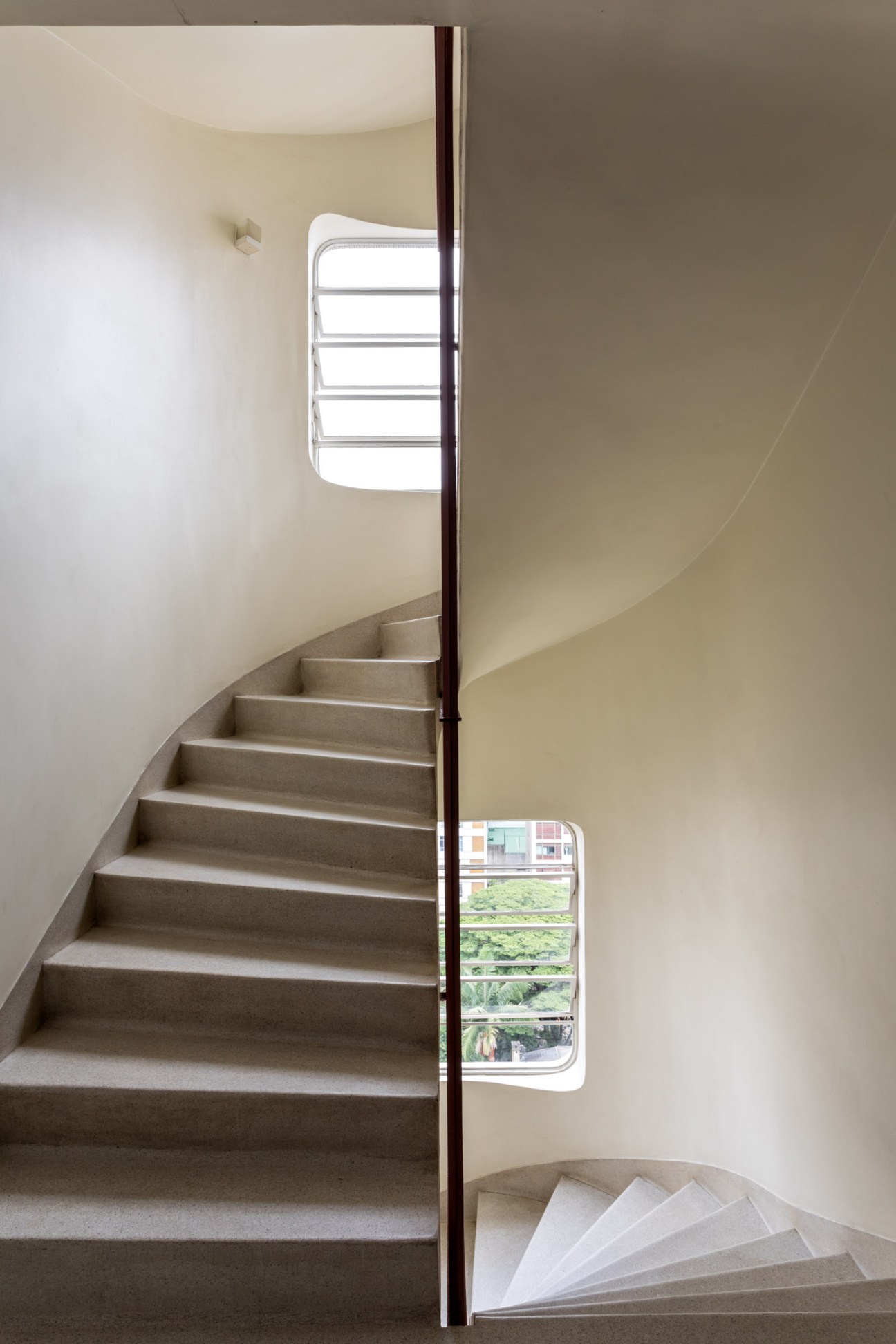 Curved concrete staircase in the Lausanne building with dark metal handrail and window with horizontal slats.