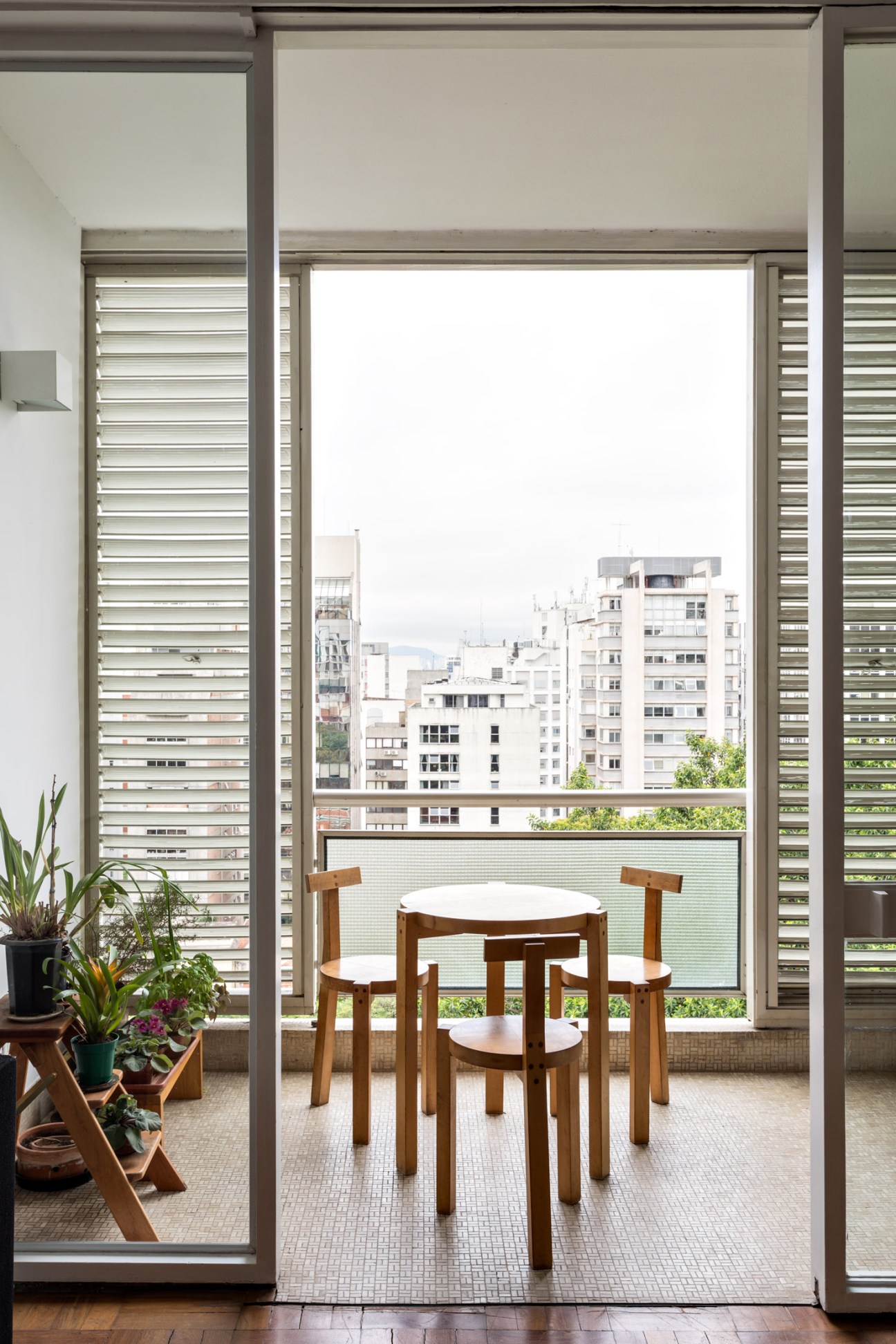 View from a São Paulo apartment balcony with modernist shutters framing a cityscape of residential buildings.