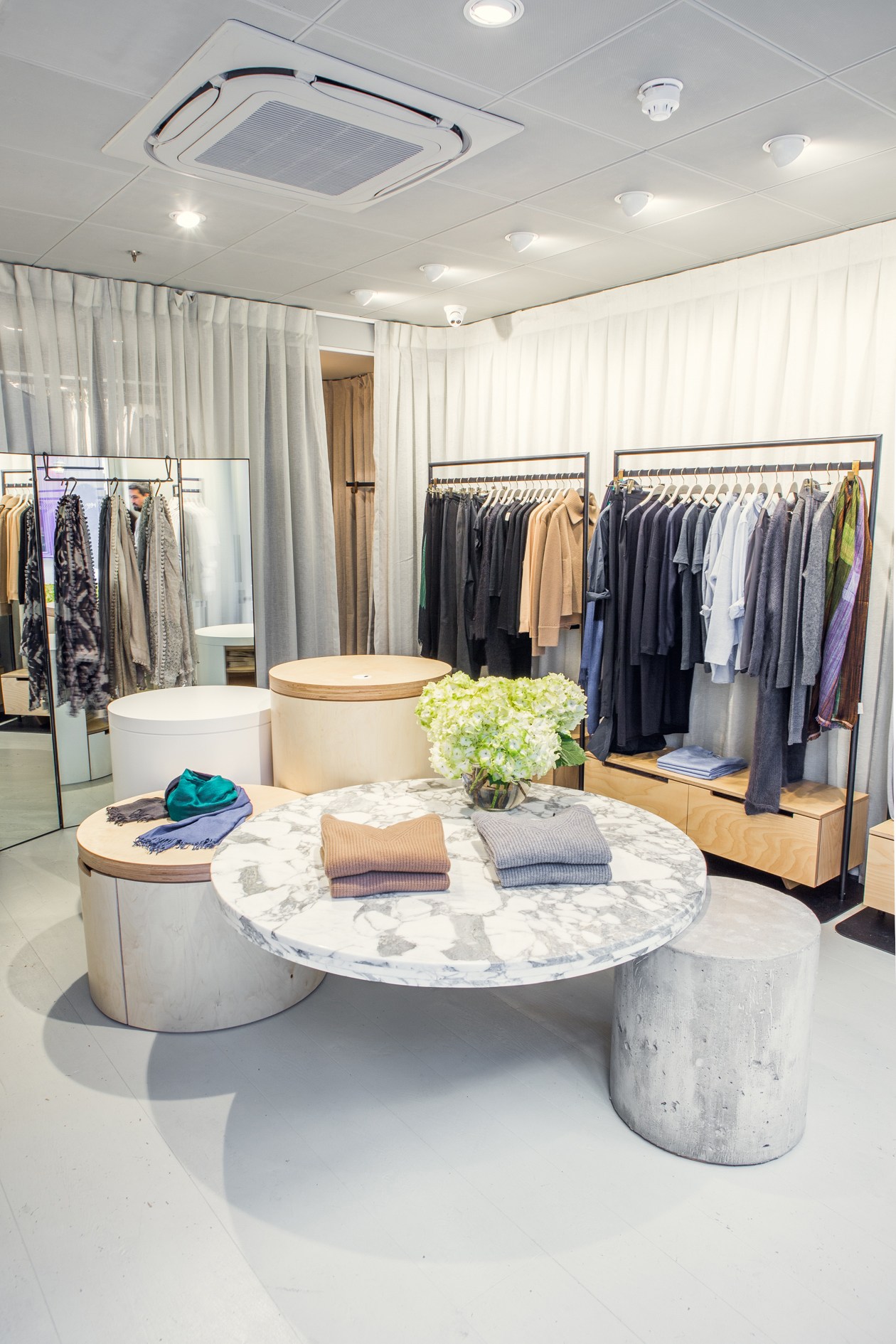 Interior of Jac+Jack store in London showing marble table display with clothing and racks of merchandise.