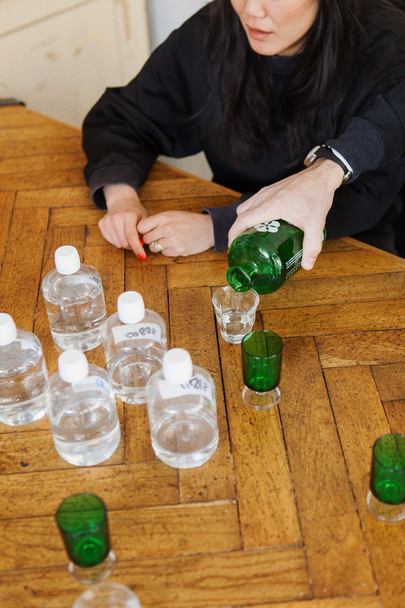Woman pouring green bottle of Wihayo soju into glasses on wooden table at Smörgåsbord studio tasting.