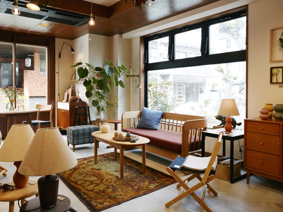 Bright, minimalist interior of Bullpen furniture shop with mid-century modern seating, wooden furniture, and potted plants by large windows.